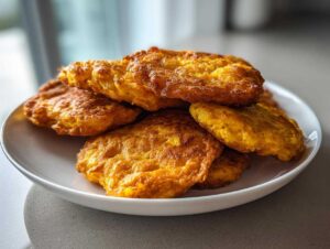 A stack of freshly fried, golden brown hot water cornbread patties piled on a white plate.