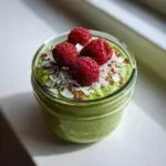 Close-up of vibrant green matcha chia pudding topped with fresh raspberries and coconut flakes.