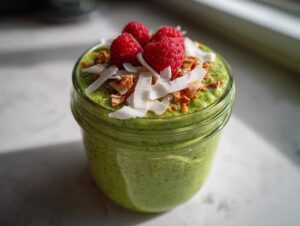 Close-up of bright green matcha chia pudding topped with fresh raspberries, coconut flakes, and granola.