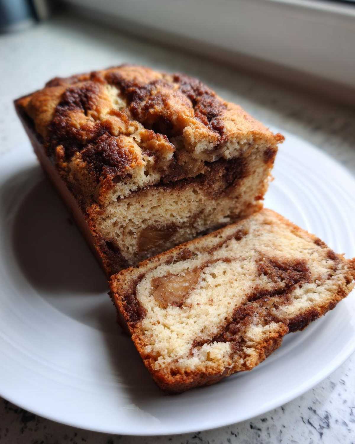 A loaf of moist apple bread, partially sliced, showing a rich cinnamon swirl and chunks of cooked apple.