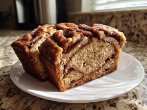 Two thick slices of moist apple bread featuring a rich cinnamon swirl, served on a white plate.
