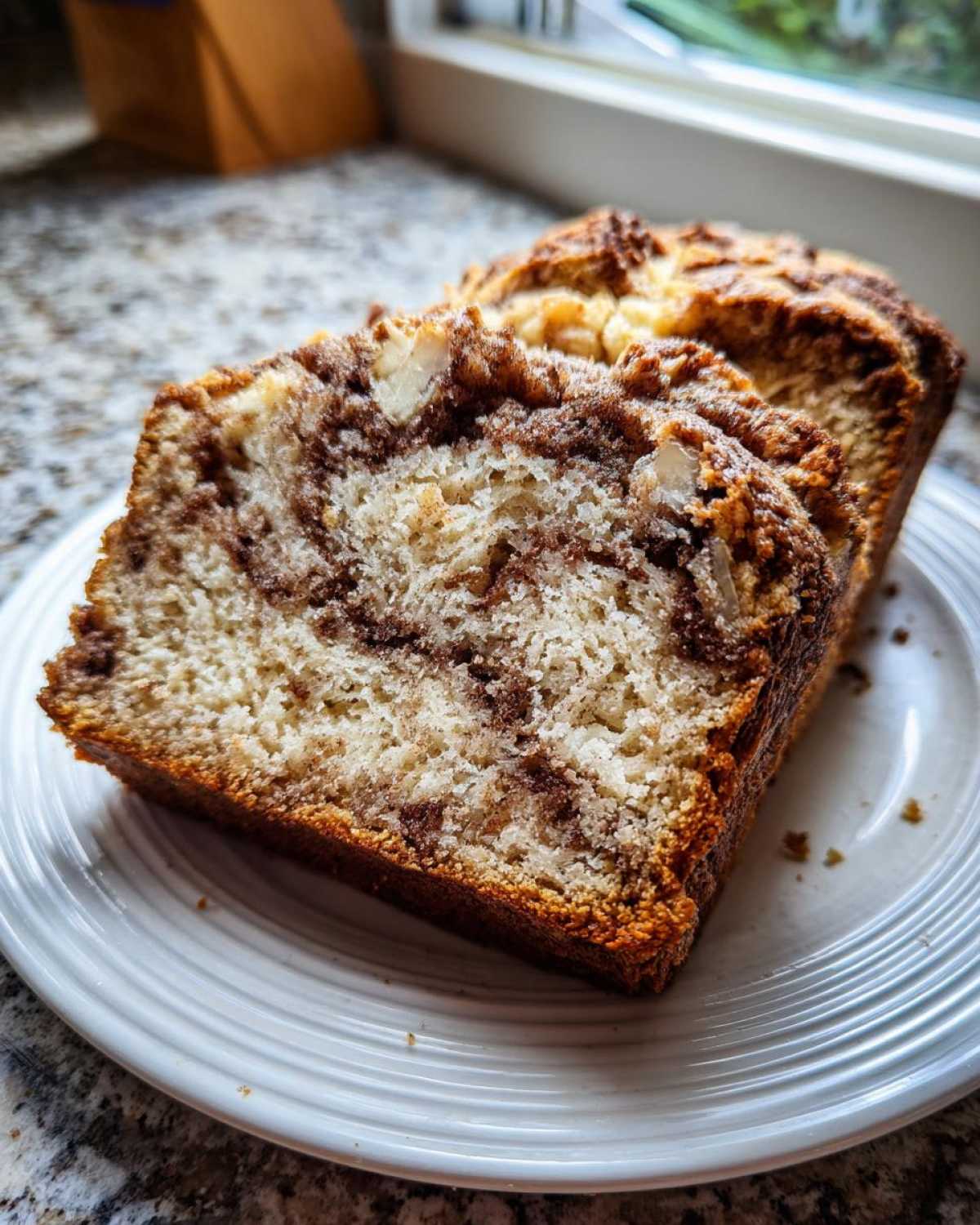 Close-up of two thick slices of moist apple bread with cinnamon swirl on a white plate.