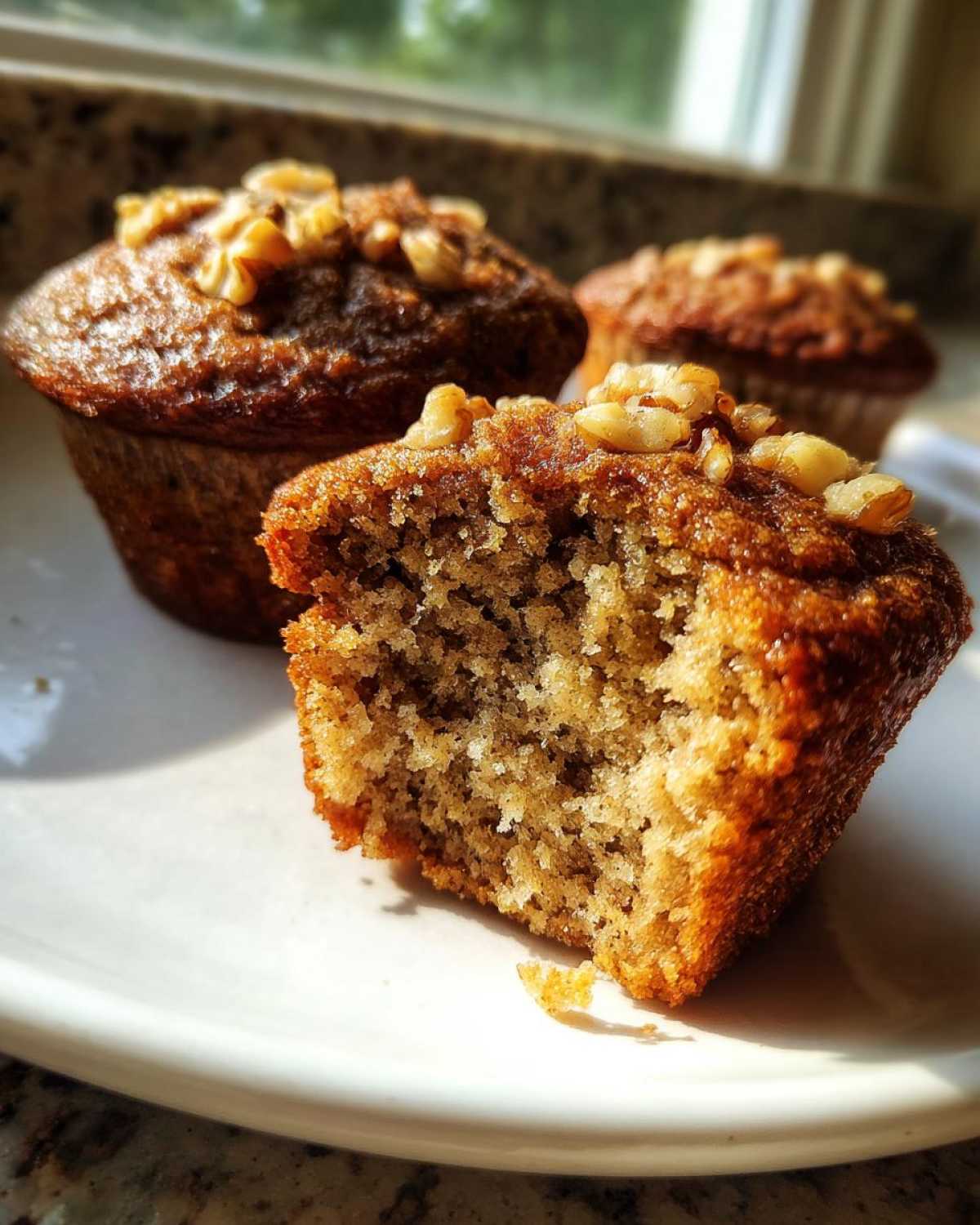 Close-up of a moist banana nut muffin with a bite taken out, showing the crumb texture and walnut topping.
