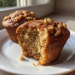 Close-up of a moist banana nut muffin with a bite taken out, showing the crumb texture and walnuts on top.