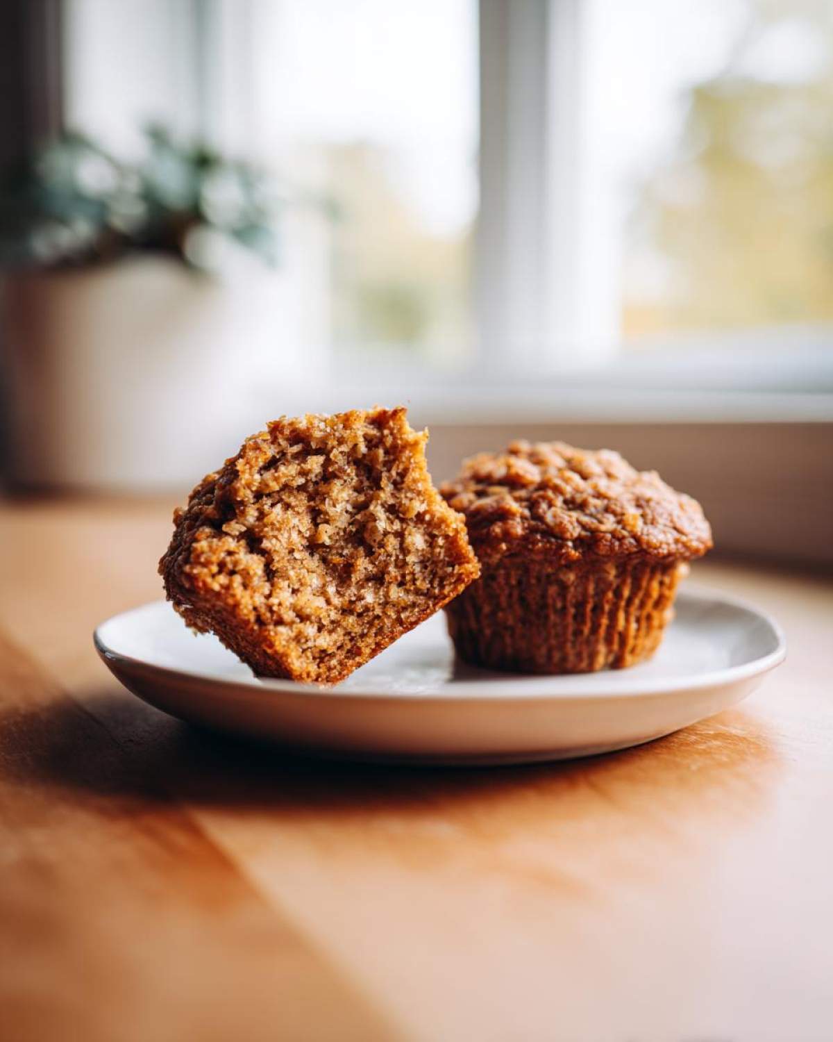Close-up of a banana oatmeal muffin cut in half showing the moist, textured interior next to a whole muffin.