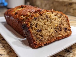 A close-up of a freshly baked loaf of greek yogurt banana bread, showing a moist interior with nuts and raisins.