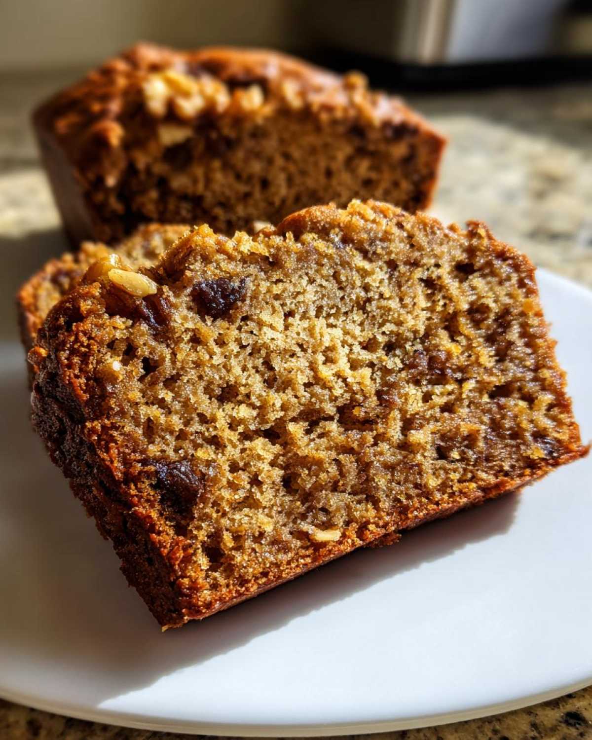 Close-up of a moist slice of greek yogurt banana bread showing texture, raisins, and nuts on a white plate.