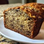 Close-up of a moist slice of greek yogurt banana bread showing a tender crumb and walnuts on top.