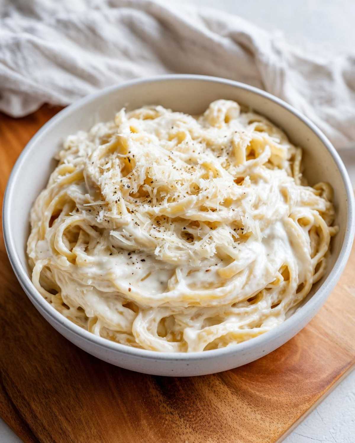 Close-up of pasta coated in a rich, white cream sauce, topped with grated cheese and black pepper.