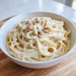 Close-up of fettuccine pasta generously coated in a rich, white cream sauce and topped with grated cheese.
