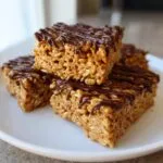 A stack of three delicious peanut butter rice krispie treats drizzled with melted chocolate on a white plate.