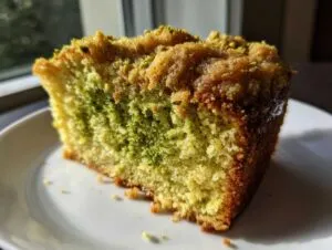 Close-up of a moist slice of pistachio coffee cake showing green pistachio swirl and golden crumb topping.