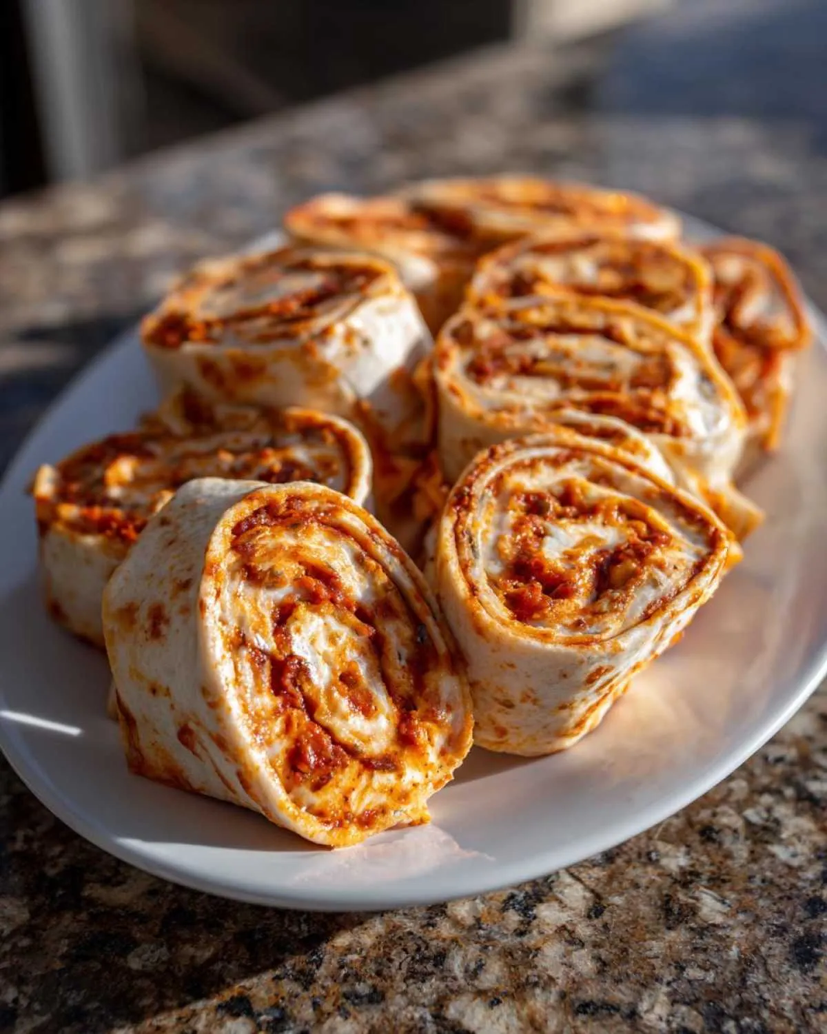 A white plate filled with freshly cut taco pinwheels featuring a swirl of red filling and cream cheese.