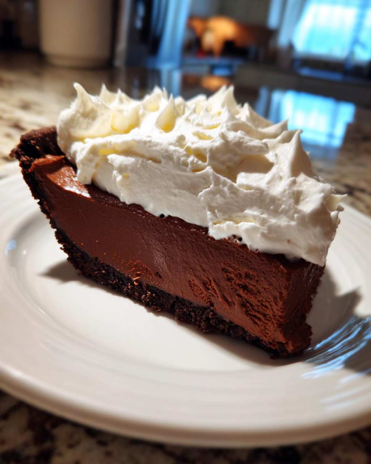 A perfect slice of chocolate cream pie featuring a dark chocolate filling and thick whipped cream topping on a white plate.