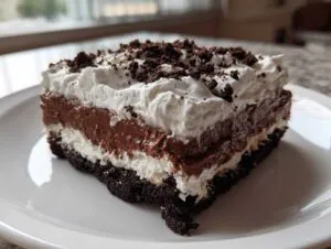 A close-up of a rich slice of chocolate lasagna featuring a dark crust, cream layer, chocolate pudding, and whipped topping.