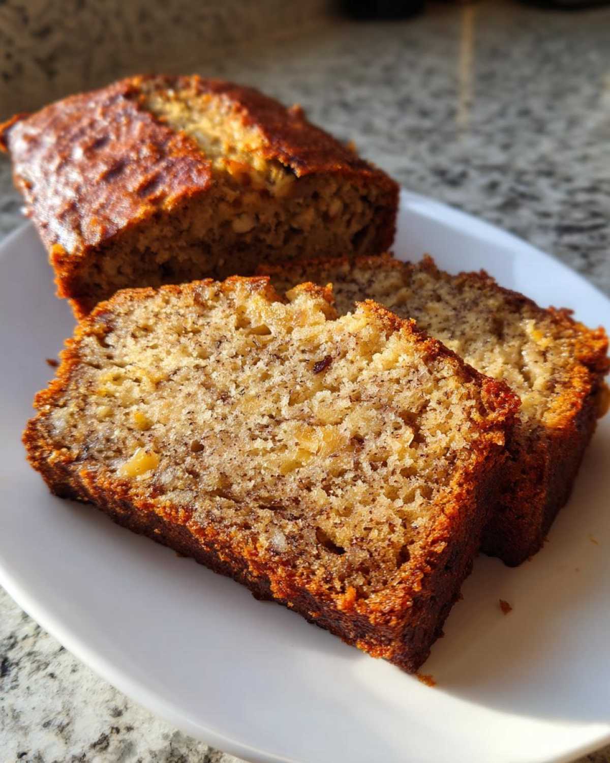 Two thick slices of moist greek yogurt banana bread with a dark, caramelized crust, resting on a white plate.