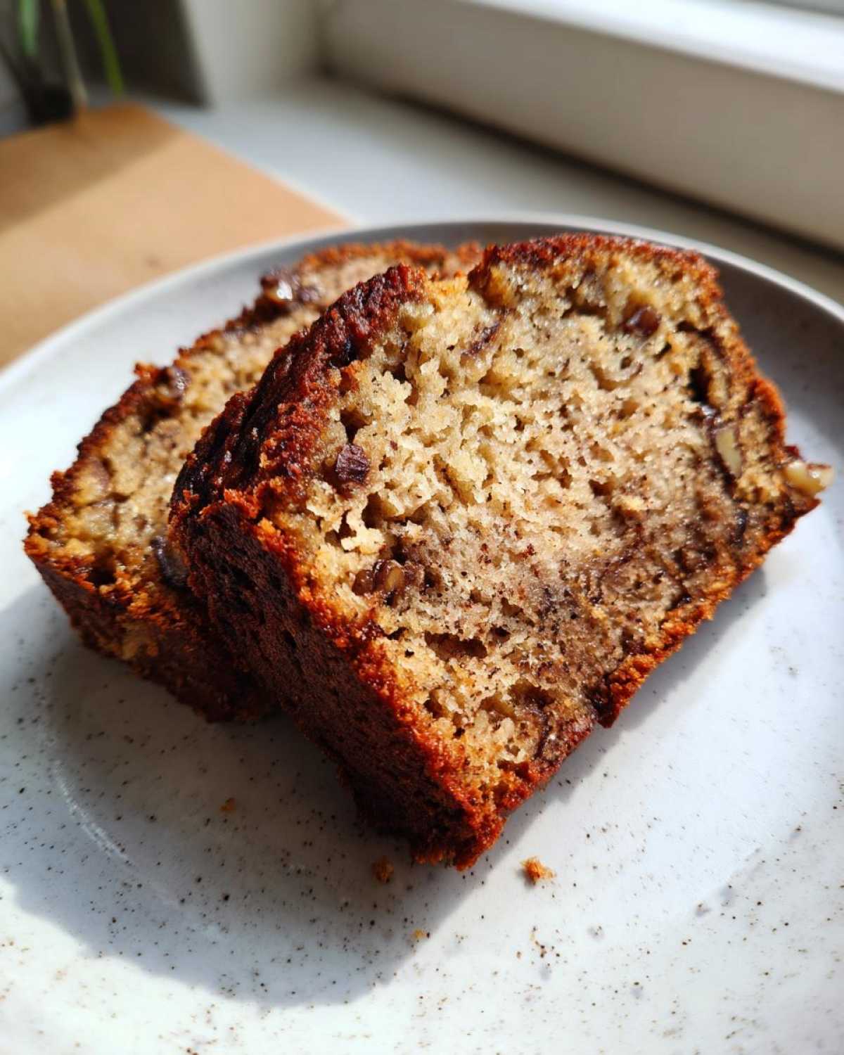 Two slices of moist sugar free banana bread with visible nuts on a speckled white plate.