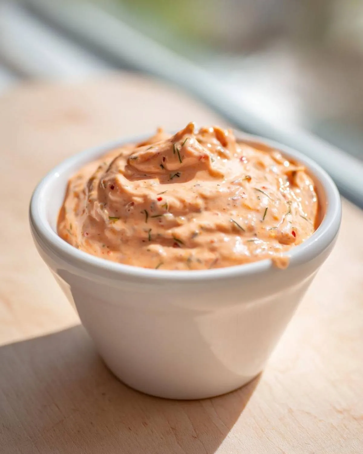 Close-up of creamy, orange-hued smash burger sauce with visible herbs and spices in a small white bowl.