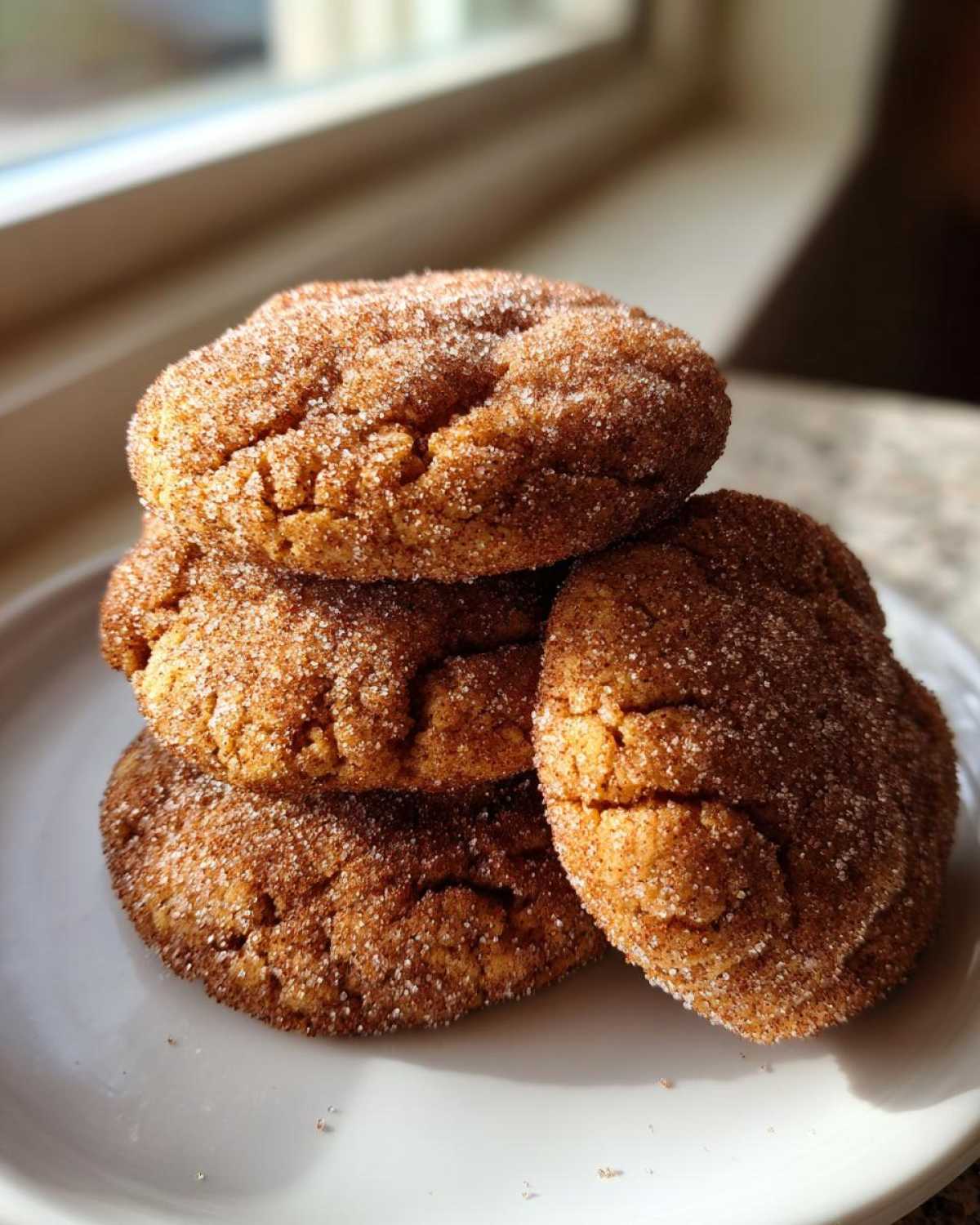 A stack of four soft, chewy cinnamon cookies generously coated in sparkling cinnamon sugar, sitting on a white plate.