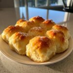 A plate of freshly baked, golden brown soft dinner rolls drizzled with a shiny glaze.