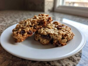 Two soft oatmeal raisin cookies, one broken in half to show the chewy interior, resting on a white plate.