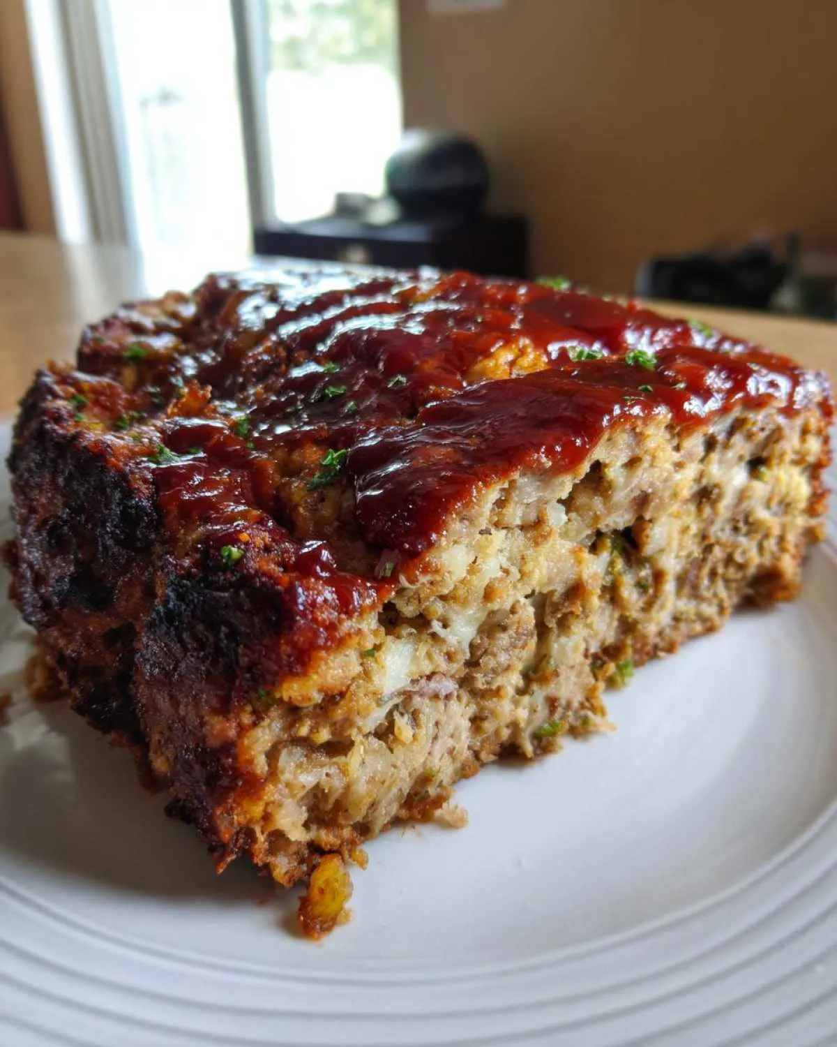 A thick slice of stove top stuffing meatloaf topped with a rich, dark glaze, served on a white plate.