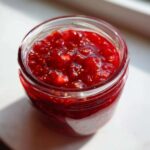 Close-up view of a glass jar filled with chunky, bright red strawberry freezer jam, showing visible seeds.