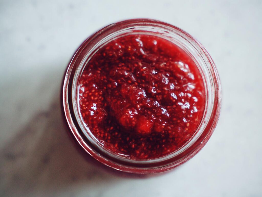 Overhead view of vibrant red strawberry freezer jam with visible seeds inside a clear glass jar.
