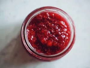 Overhead view of vibrant red strawberry freezer jam with visible seeds inside a clear glass jar.