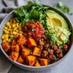 A vibrant sweet potato taco bowl featuring roasted sweet potatoes, seasoned ground meat, corn, salsa, avocado, and fresh cilantro.