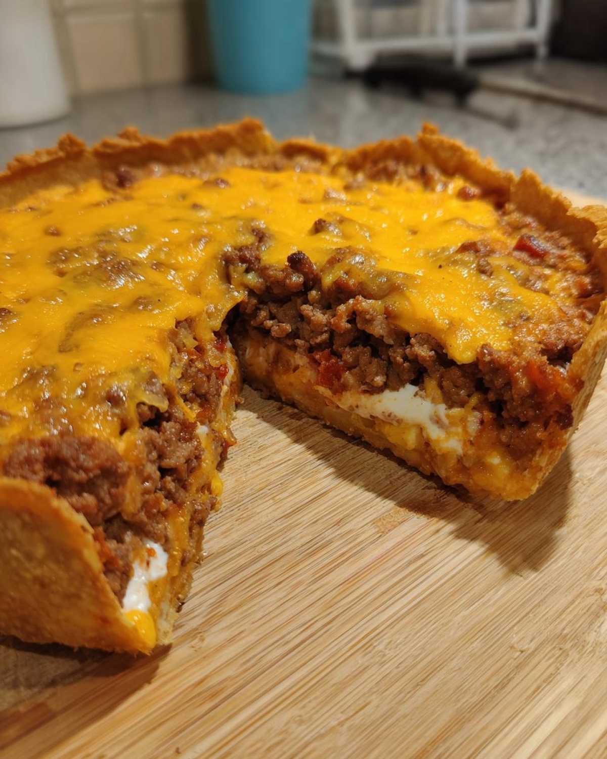 Close-up of a freshly baked taco pie with a slice removed, showing layers of seasoned meat and cheese topping.