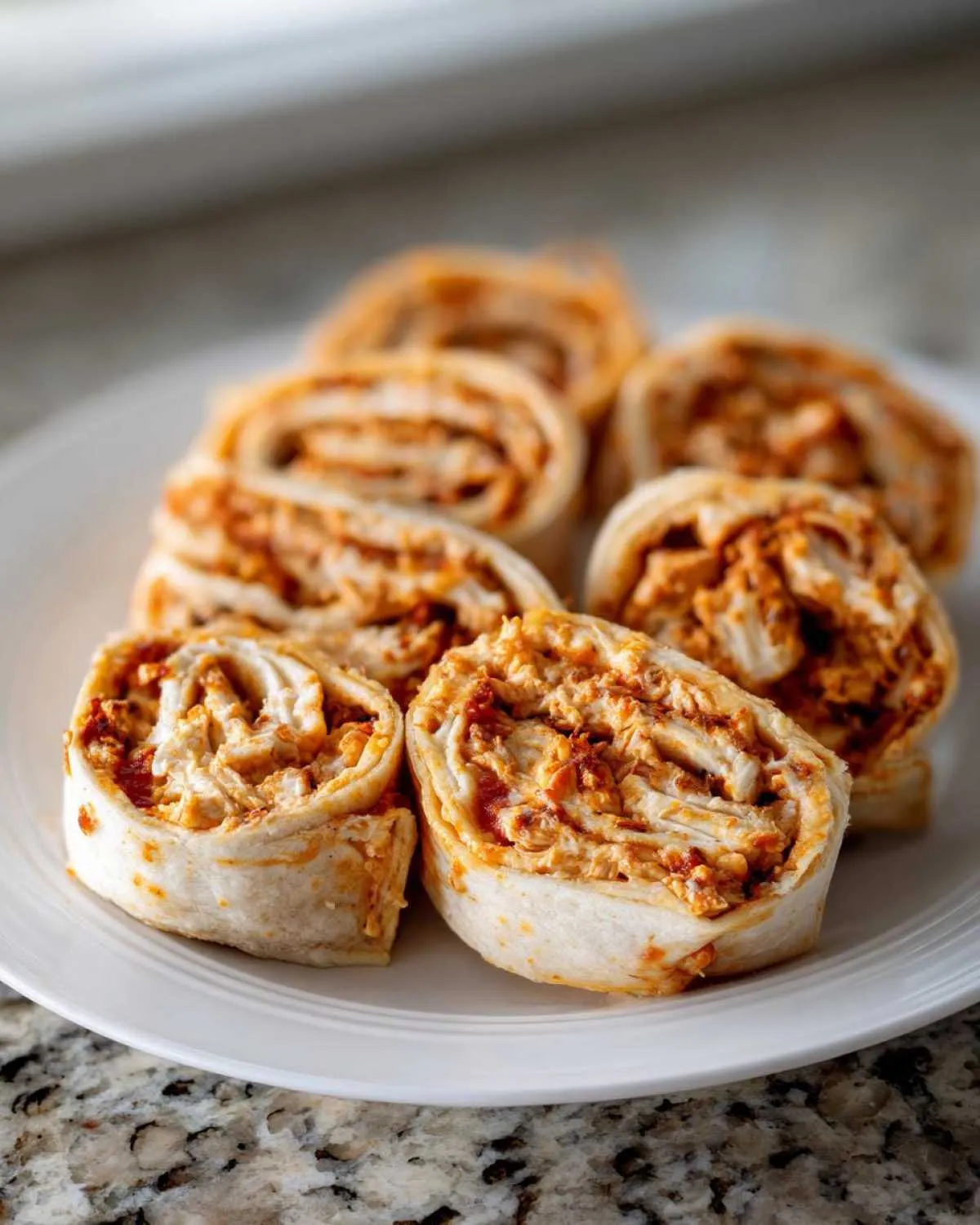 A close-up shot of several savory taco pinwheels filled with shredded chicken and sauce, arranged on a white plate.
