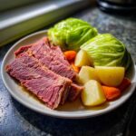 A plate featuring tender slices of corned beef and cabbage, alongside boiled potatoes and carrots.