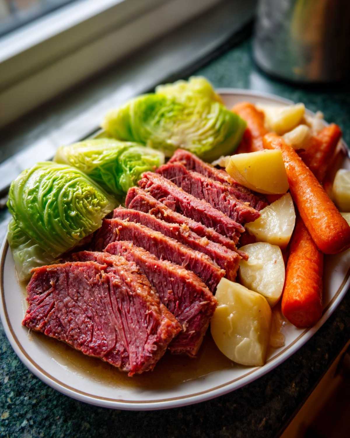 Slices of tender corned beef and cabbage served with boiled carrots and potatoes.