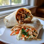 Close-up of a thai peanut chicken wrap cut in half, showing shredded chicken, slaw, and peanut sauce.
