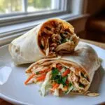 Close-up of a thai peanut chicken wrap cut in half, showing shredded chicken, slaw, and peanut sauce.