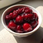 Close-up of thick, glossy cherry pie filling with whole, bright red cherries in a white bowl.