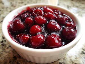 Close-up of thick, glossy cherry pie filling with whole cherries in a small white ramekin.