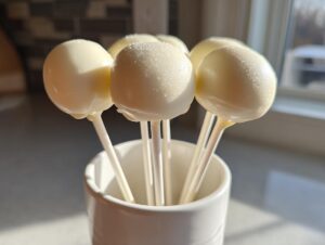 A cluster of homemade white chocolate cake pops standing upright in a white mug.