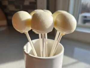 A cluster of homemade white chocolate cake pops standing upright in a white mug.