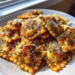 A pile of golden brown, crispy air fryer cheesy ravioli sprinkled generously with grated parmesan cheese and herbs.