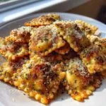 A pile of golden brown, crispy air fryer cheesy ravioli sprinkled generously with grated parmesan cheese and herbs.