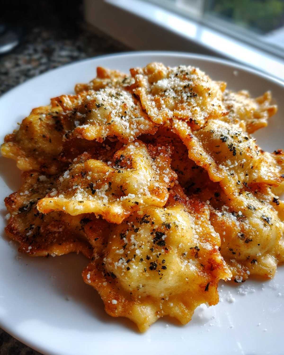 A pile of golden brown, crispy air fryer cheesy ravioli dusted with grated parmesan and dried herbs on a white plate.