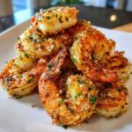 A pile of golden brown, crispy air fryer garlic parmesan shrimp seasoned with parsley on a white plate.