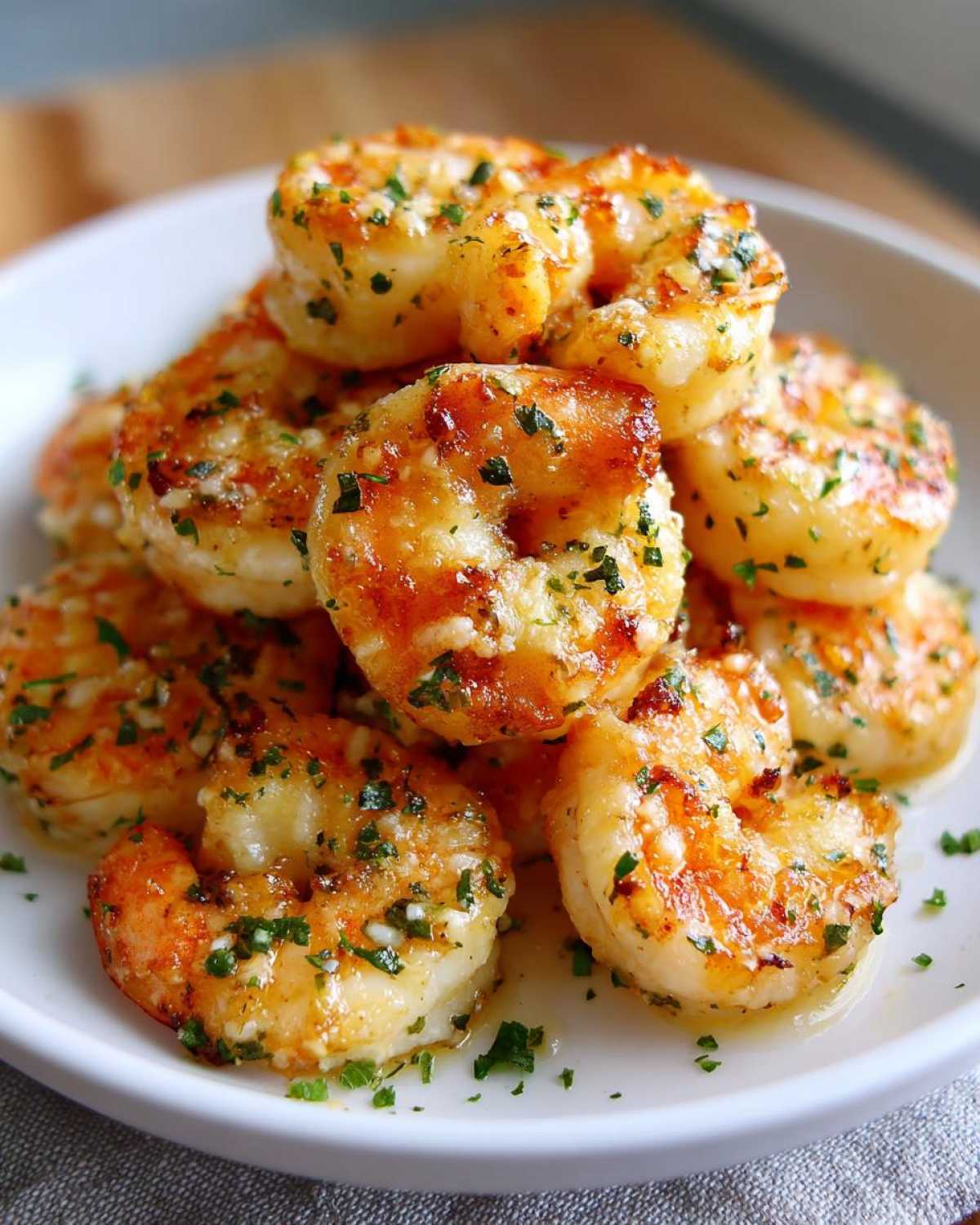 Close-up of perfectly cooked air fryer garlic parmesan shrimp piled high on a white plate, glistening with butter and herbs.