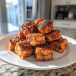 A pile of perfectly cooked, crispy, seasoned air fryer salmon bites stacked high on a white plate.