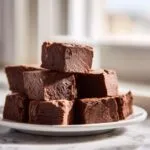 A tempting stack of rich, dark chocolate fudge squares piled high on a white plate.