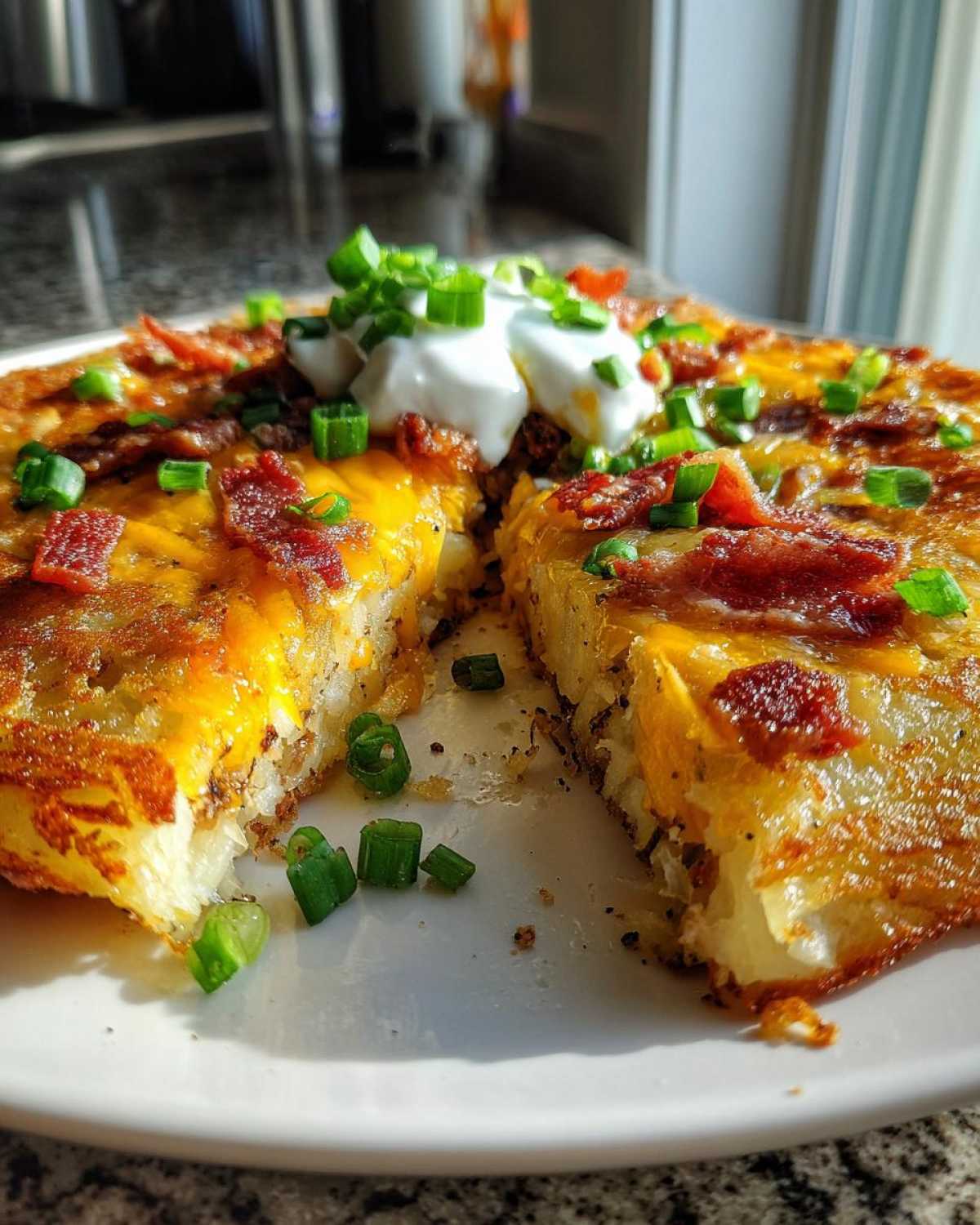 A cross-section view of amazing 3-ingredient loaded hash browns topped with melted cheese, bacon, sour cream, and green onions.