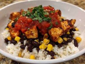 A close-up of an amazing chicken burrito bowl featuring seasoned chicken, black beans, corn, rice, salsa, and cilantro.