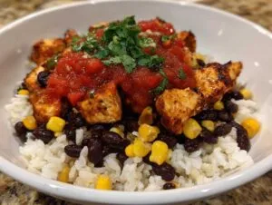 A close-up of an amazing chicken burrito bowl featuring seasoned chicken, black beans, corn, rice, salsa, and cilantro.